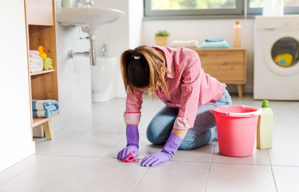 ผู้หญิงกำลังขัดยาแนวห้องน้ำ ด้วยผลิตภัณฑ์ทำความสะอาดที่อาจทำให้ยาแนวกร่อน